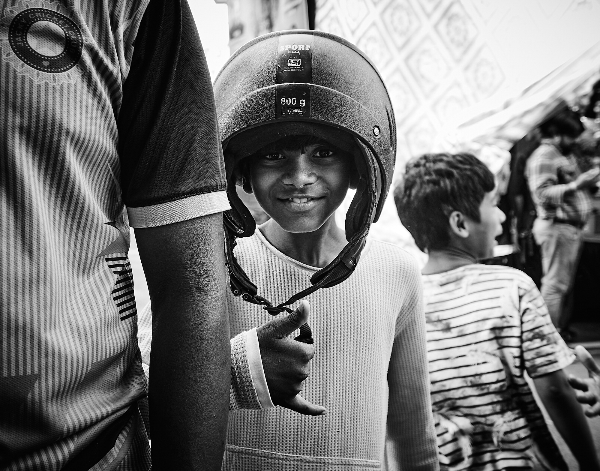ムンバイでヘルメットをかぶり笑顔を向ける少年のモノクロ写真