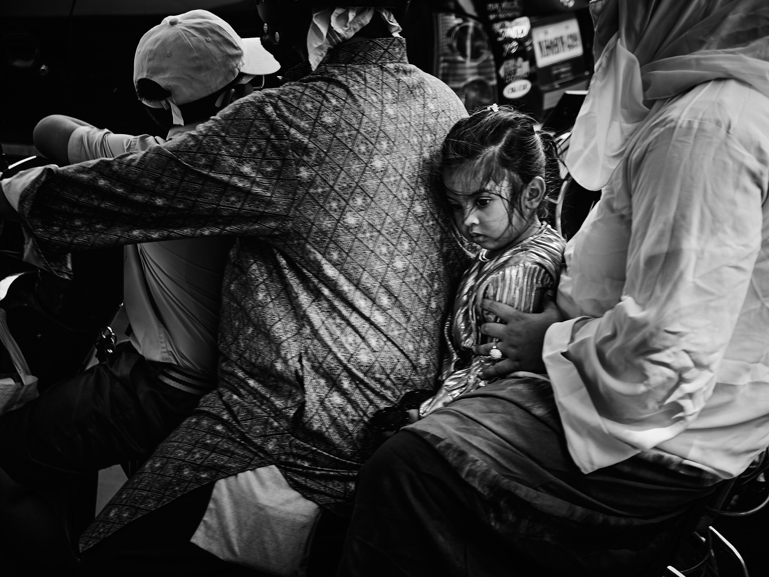 ムンバイの乗り物の中で、大人たちに囲まれて座る少女のモノクロ写真